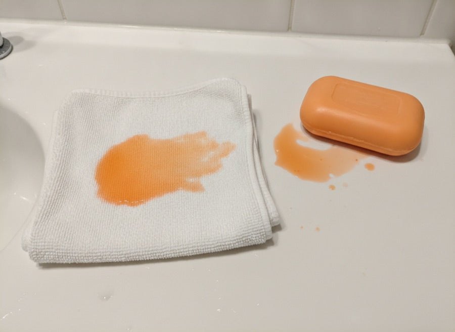 En orange fläck av färgämne på en vit tvättlapp bredvid en tvål